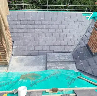 Roof partially tiled with slate during construction, with brick chimney visible.