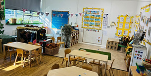 Brightly lit early years classroom with wooden tables and chairs.