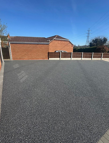 Newly installed tarmac driveway with brick and concrete borders, under blue sky.