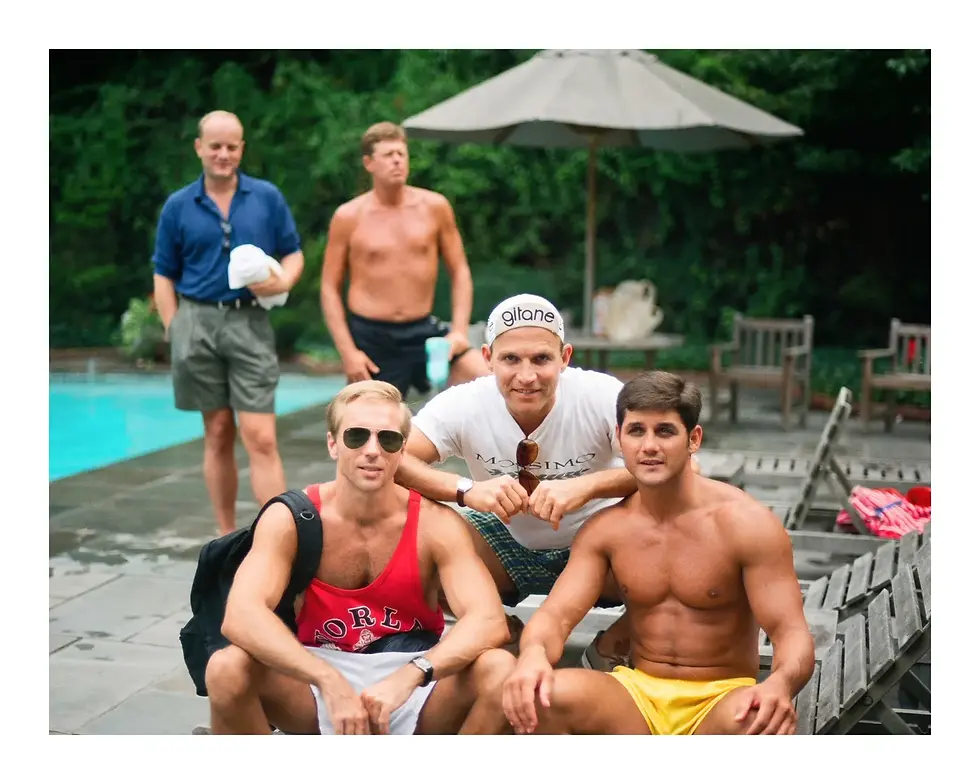 Five men posing poolside. Three men sit and crouch in the foreground: one in sunglasses and a red tank top, one in a white Gitane cycling cap, and one shirtless in yellow swim trunks. Two men stand in the background next to a pool and trees.