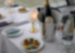 Elegant table set with a champagne bottle in an ice bucket, a small plate of appetizers, two glasses, a water bottle, and a lit lamp.