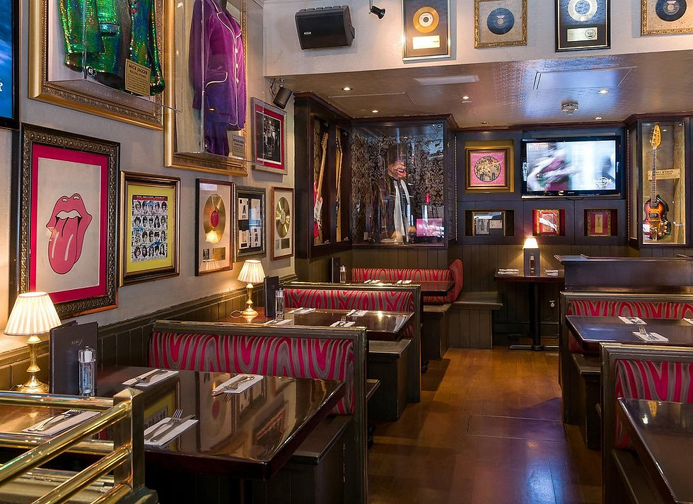 Cozy diner with red-striped booths, in Hard Rock Cafe, London, framed records, and music memorabilia on walls. Warm lighting and a TV in the background.