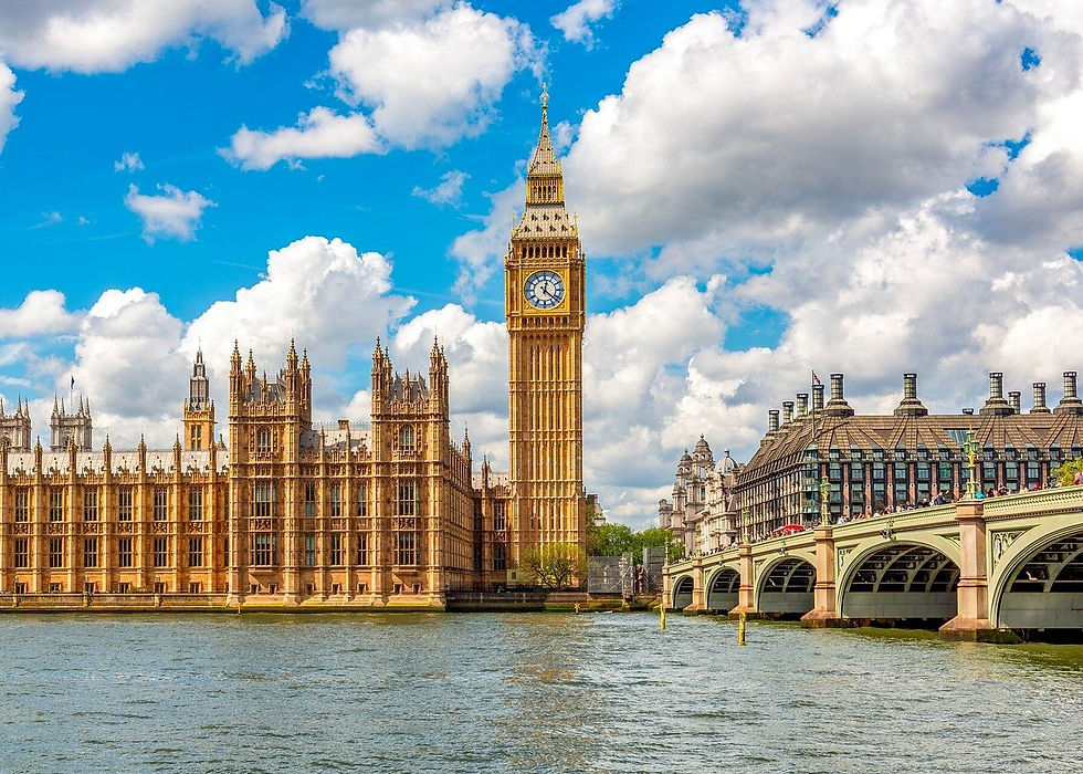 Big Ben and the Houses of Parliament under a blue sky with clouds, next to the River Thames and Westminster Bridge. Bright and vibrant scene.