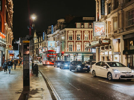 Night view of Regent Street in London, illuminated with bright street lights and shop displays, with a red double-decker bus.