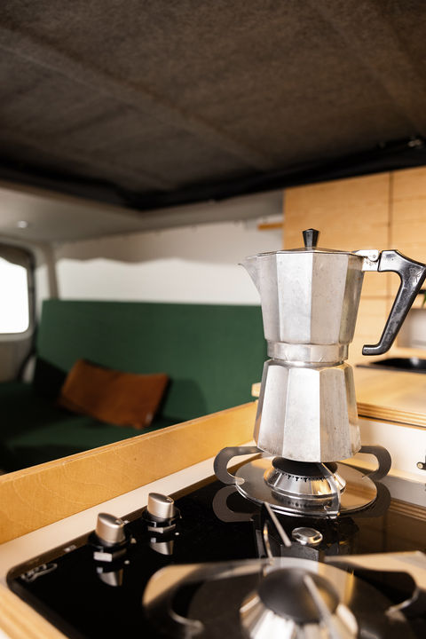 Gezellige camperkeuken met een gaskookplaat en een percolator, gecombineerd met een comfortabele zithoek