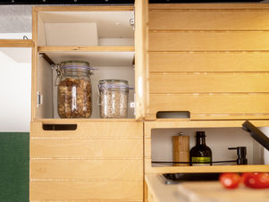 Open houten keukenkastjes in een bestelbus omgebouwd naar camper, gevuld met glazen potten met etenswaren