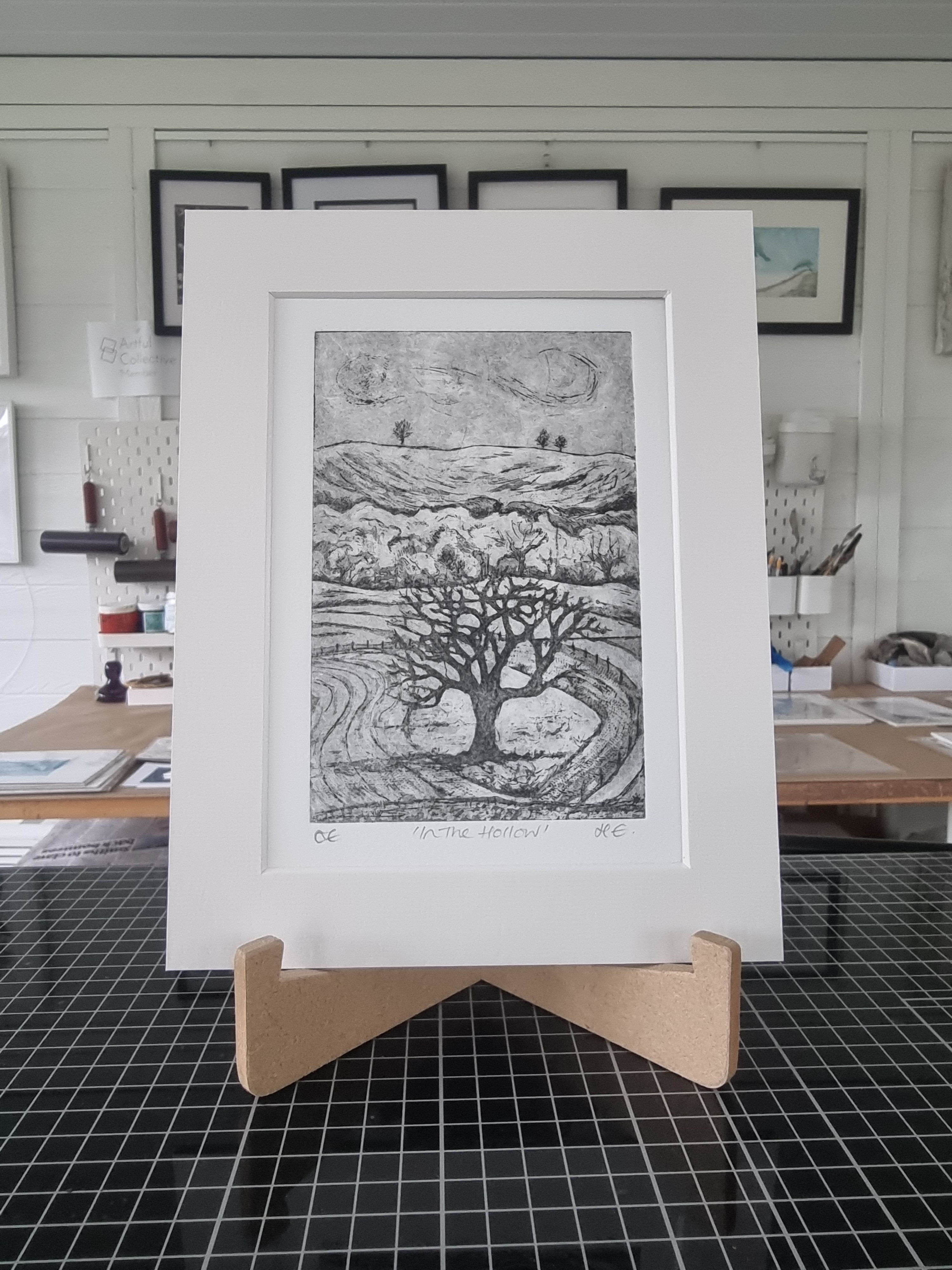 Small monochrome etching of a Tree in a Hollow with a rising hill behind it.