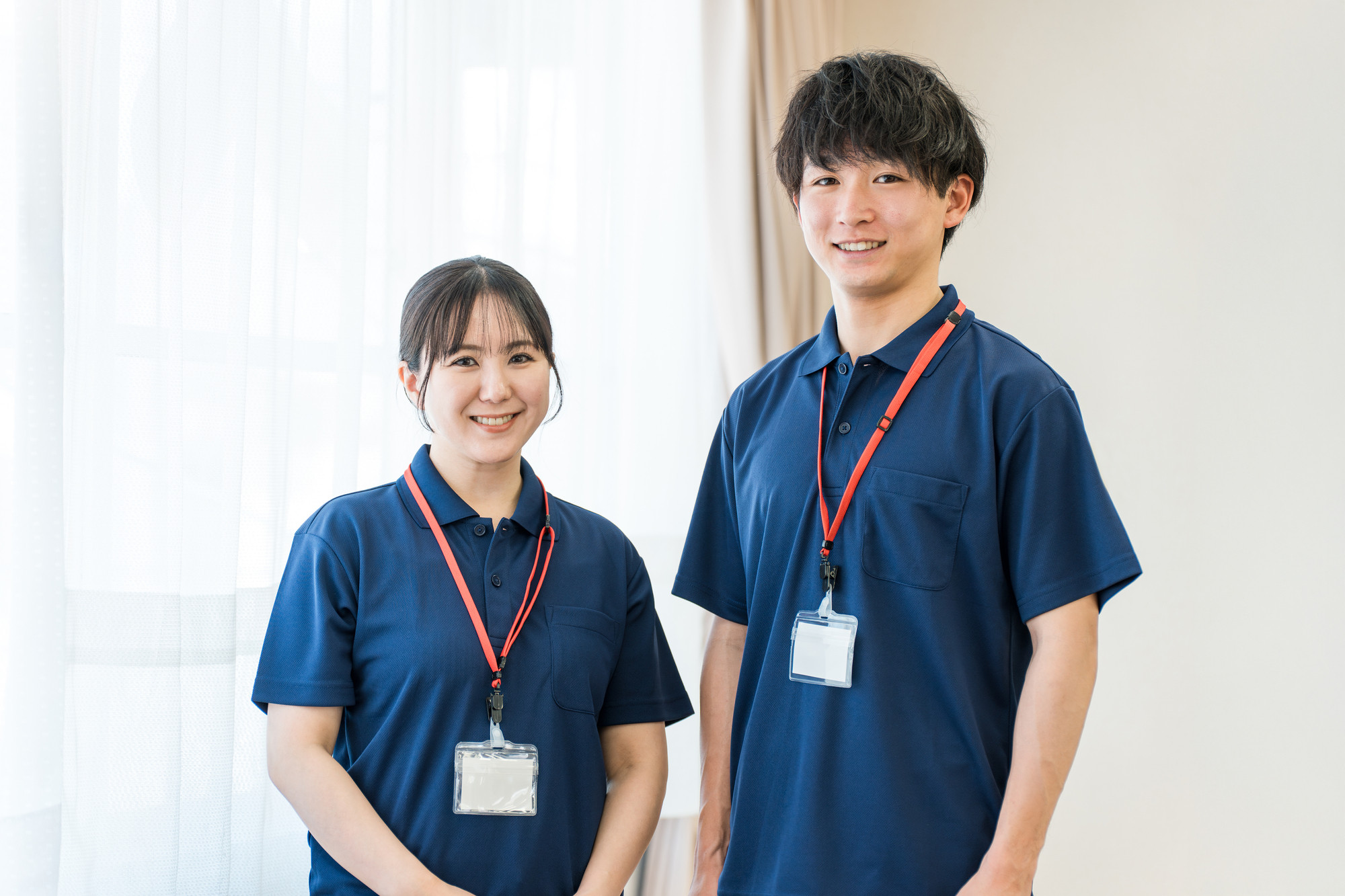 介護施設のスタッフ2名が制服と身分証を着用して立っている