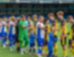 Newcastle Town and Bury players exchange handshakes at Gigg Lane ahead of the Northern Premier League fixture on Saturday 9th August 2025
