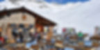 Mountain chalet restaurant with outdoor seating in St. Moritz, surrounded by snowy slopes and skiers enjoying a sunny winter day.