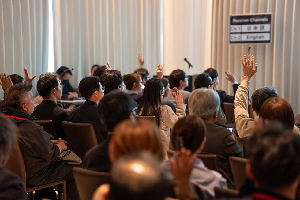 カンファレンス会場で、多数の参加者が手を挙げて発言を求める。背活発な雰囲気。