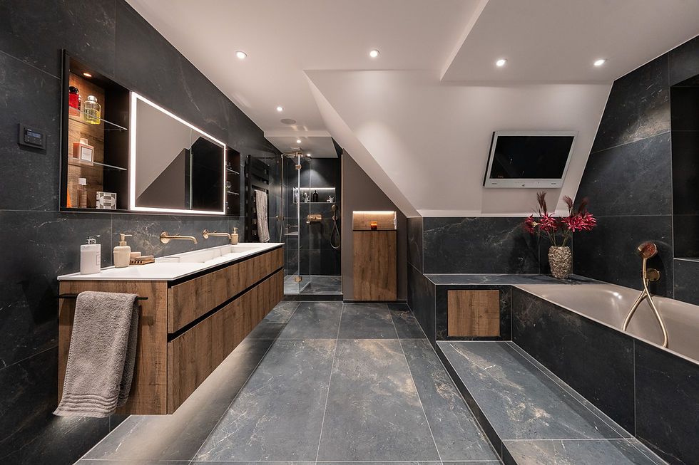 Exklusive Badausstattung in Hamburg: Luxuriöses Badezimmer mit großformatigen dunklen Natursteinfliesen, hochwertigem Waschtisch in Holzoptik, integriertem TV und stimmungsvoller Beleuchtung – präsentiert von BAD ELEMENTE.