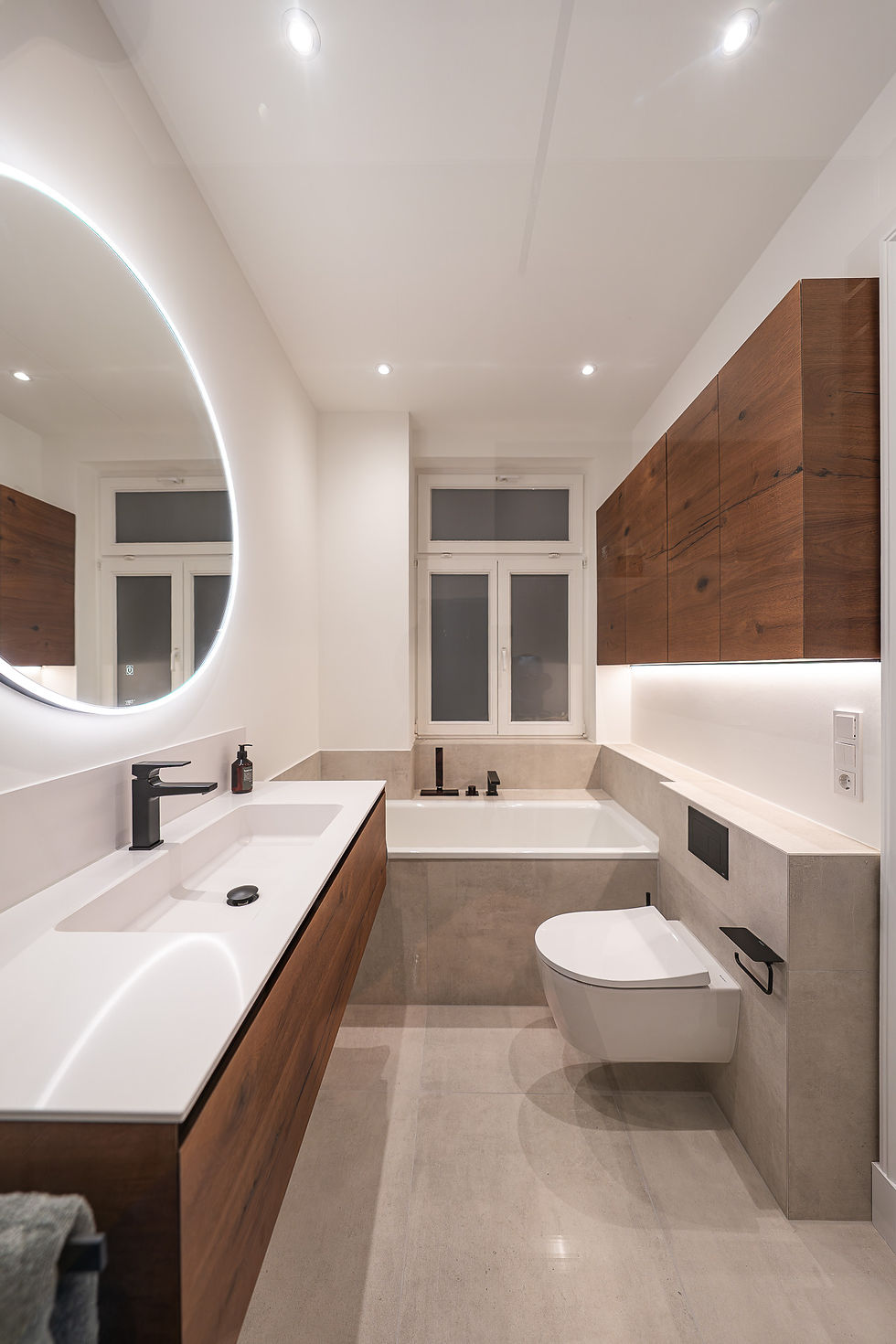 Exklusive Neubau-Veredelung in Hamburg: Modernes Badezimmer mit Doppelwaschtisch, beleuchtetem Rundspiegel, freistehender Badewanne und maßgefertigten Holz-Badmöbeln – individuelle Badezimmer-Ausstattung von BAD ELEMENTE.