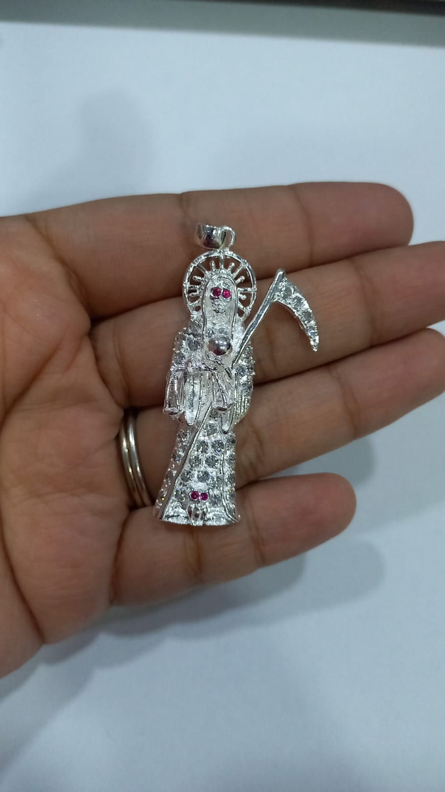 Hand holding a silver pendant of Santa Muerte with a Ring. Taxco by Design.