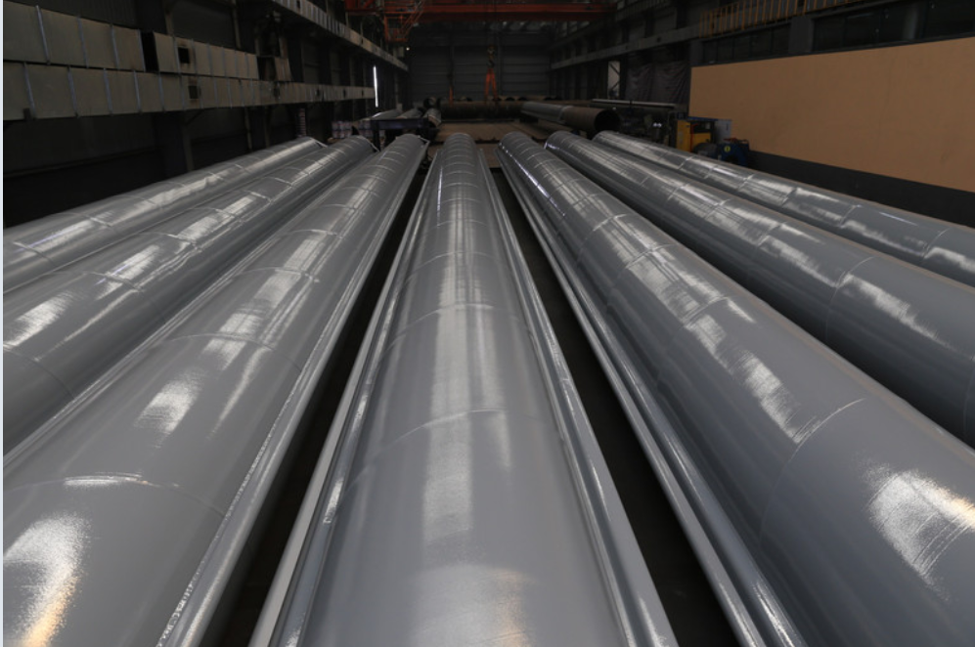 Corrosion-coated steel pipe piles stored in a fabrication facility, ready for deployment in marine, offshore, bridge, and civil infrastructure projects requiring long-term steel protection.