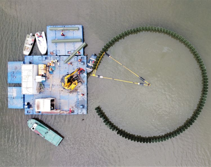 view of vinyl sheet piles forming a circular enclosure in water, creating an artificial island for bird habitat construction beside a floating work platform.