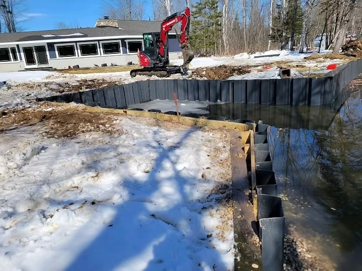 Instalación de un muro de contención de tablestacas de vinilo a lo largo de una costa nevada