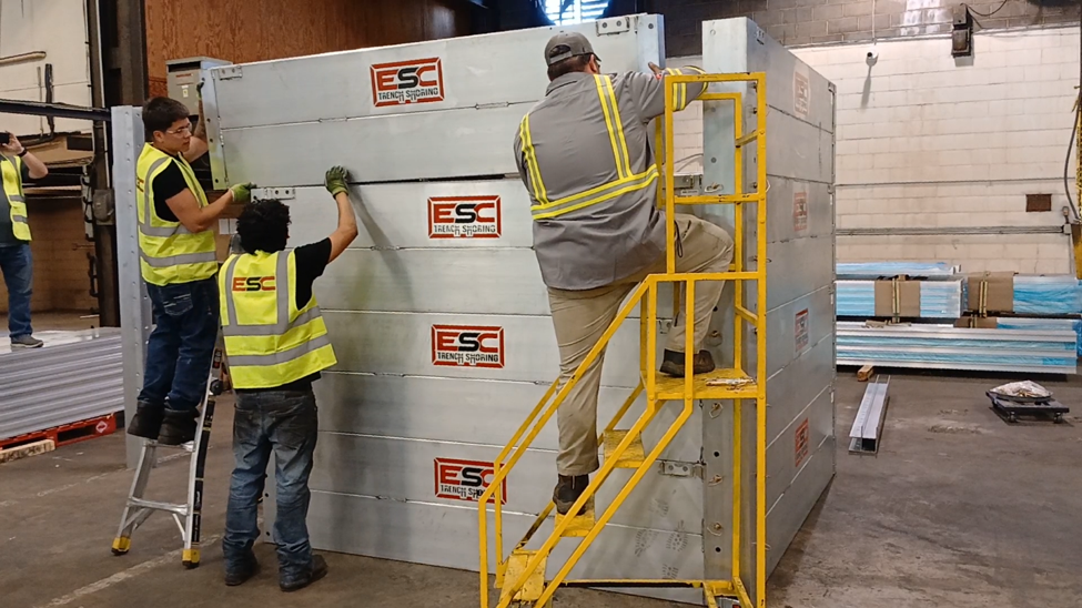 Workers assembling an ESC aluminum modular trench box system with integrated access stairs, demonstrating modular trench safety solutions for excavation projects.