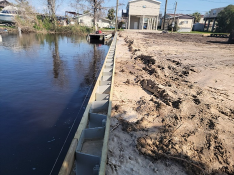 Barrera de tablestacas en construcción al lado de un muelle, reforzando la línea de costa durante las tareas de paisajismo y excavación.