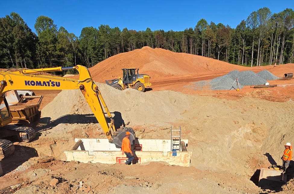 Excavation site with ESC trench box installed and heavy Komatsu equipment assisting workers, demonstrating secure shoring solutions for deep trench safety