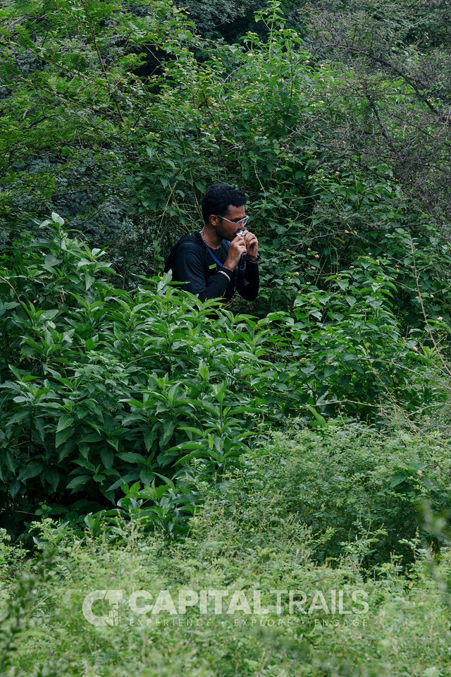 male runner in black top emerging out of a forest bush taking his gel