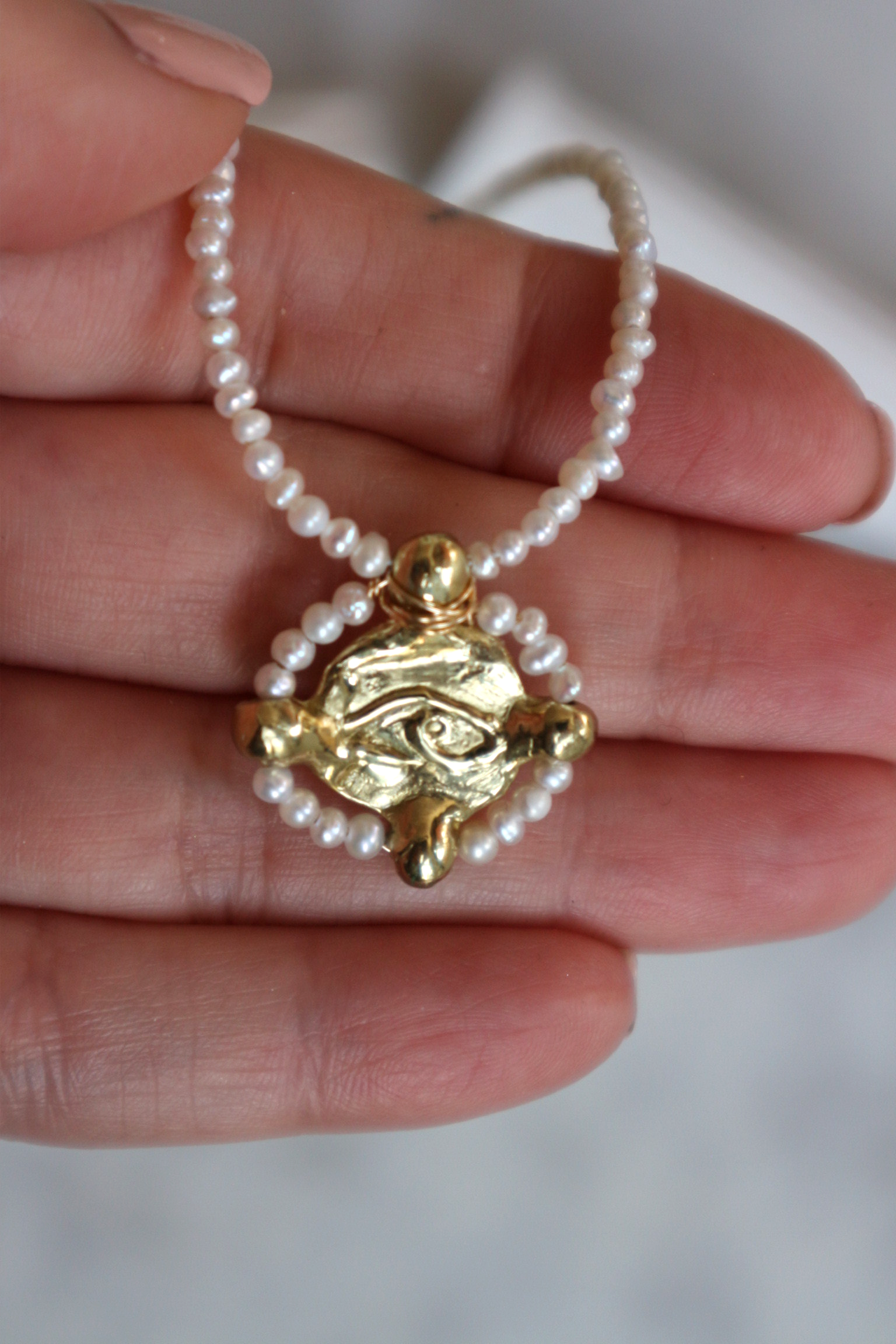 detail view of evil eye charm shown with delicate pearls around the charm