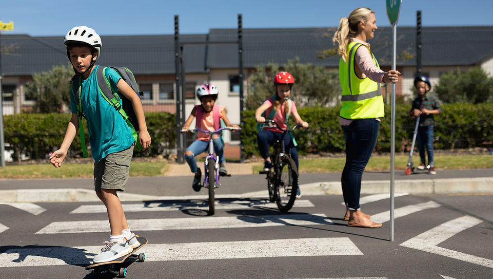 Children on skateboard and bikes going to school and a lollipop lady on the school crossing.