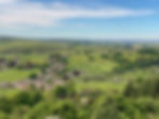 Aerial view of a Eyam Peak District mid lush green fields and scattered trees under a partly cloudy blue sky. Peaceful scene.
