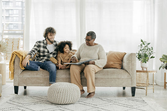 Multi-generational family reading a book together on a sofa.
