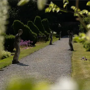 View down a wide pathway lined with plants and statues at regular intervals