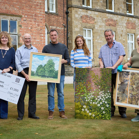 Month of Art Winners building holding their framed paintings and a giant Hopton Hall Month of Art cheque, smiling.