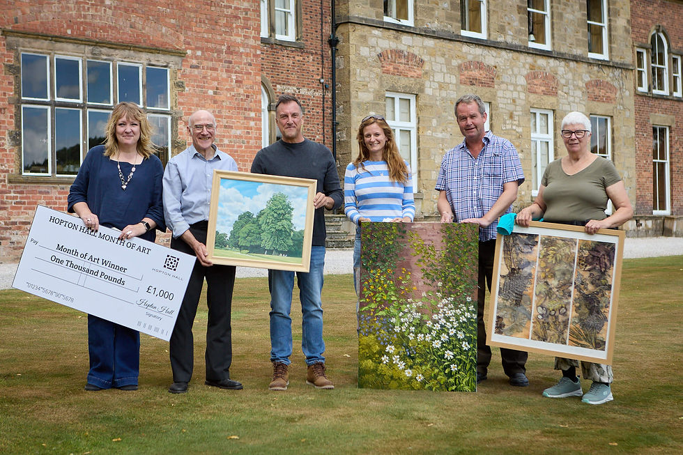 Month of Art Winners building holding their framed paintings and a giant Hopton Hall Month of Art cheque, smiling.