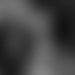 A woman breastfeeds an infant on the left while a toddler nurses from her right breast. The black and white setting is intimate and serene.