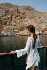 a woman in a white shirt looking at the ocean and cliffs