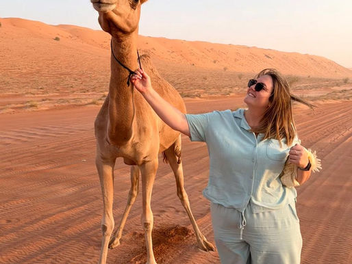 A woman in the desert holding on to the reign of a camel
