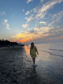 a woman walking along the shore at sunset