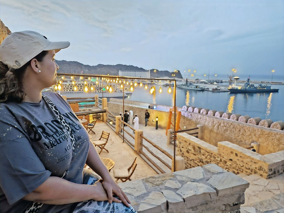 women in a white cap sitting looking out over dusk in a harbour setting