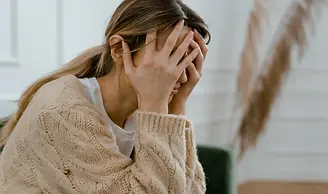 A young woman sitting with her hands over her face