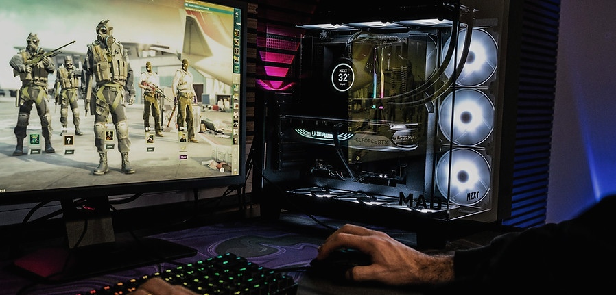 A high-performance custom gaming PC setup featuring a clean desktop computer tower with bright white RGB fans, a mechanical keyboard, and a monitor displaying gameplay.