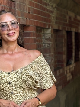 Woman standing under a stone bridge in Central Park, New York, wearing a leopard-print dress. Shoulders back, smiling softly, embodying calm confidence and self-assurance after a season of healing.
