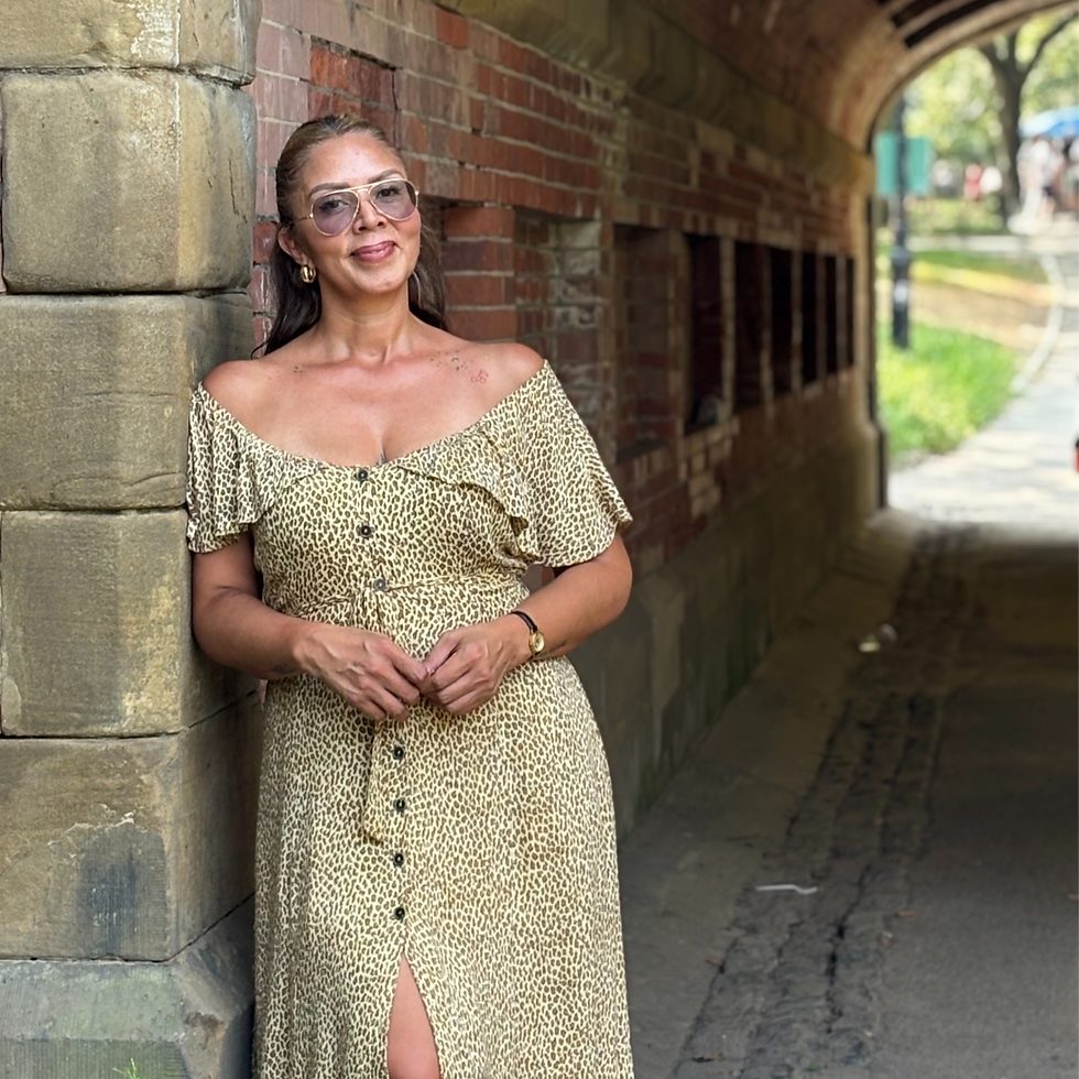 Color photo of the same woman in the same leopard-print dress, smiling brightly while leaning against a brick archway outdoors. Her posture is confident and relaxed, radiating strength and joy.