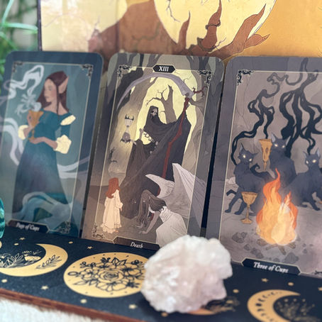 Three tarot cards depict mystical scenes with a woman, a hooded figure, and wolves. Background features a glowing light, crystals, and moons.