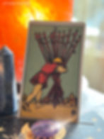 A tarot card with a figure carrying ten wands is set against an orange glowing background, featuring a crystal and celestial design.