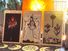 Three tarot cards titled "Tres de Espadas," "Reina de Espadas," and "Tres de Bastos" on a decorative mat, with a glowing orange lamp behind.