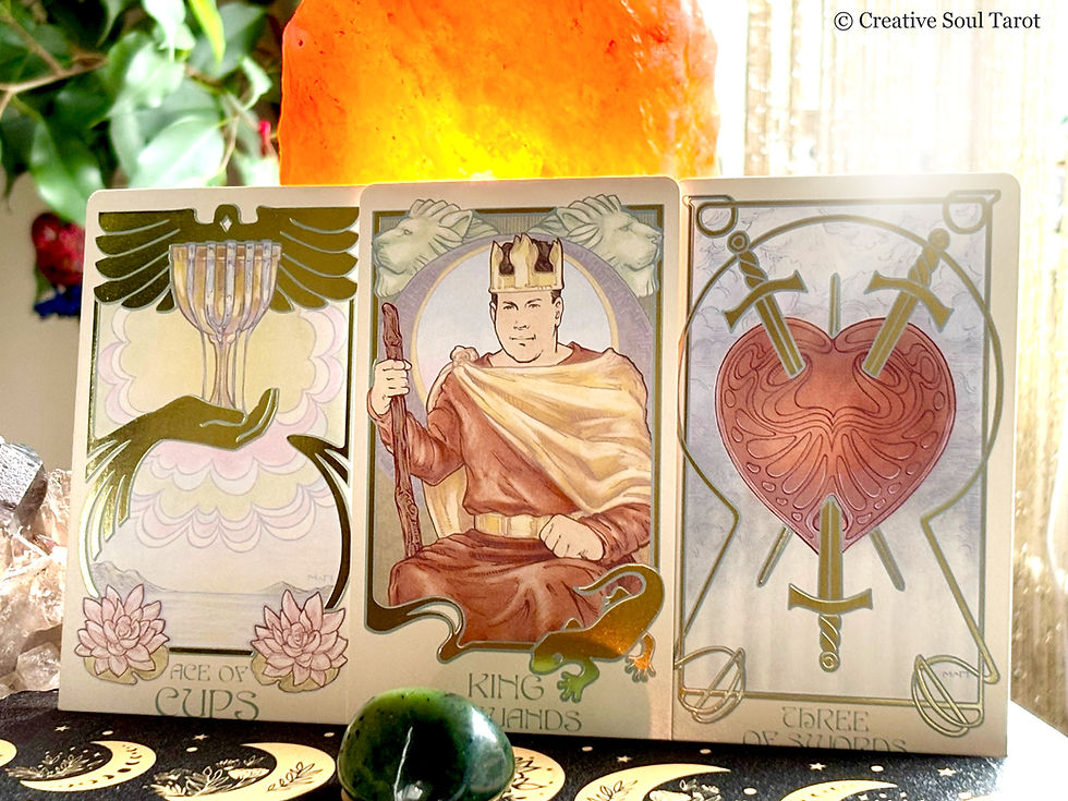Three tarot cards: Ace of Cups, King of Wands, and Three of Swords. Set against a warm light, with green foliage in the background