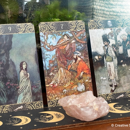 Three tarot cards, with detailed illustrations, placed beside a rose quartz stone on a decorative moon-patterned mat.