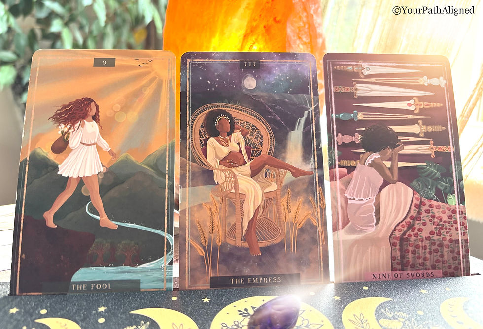 Three tarot cards, The Fool, The Empress, and Nine of Swords, lit by sunlight on a patterned cloth.