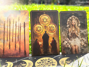 Three tarot cards on grass: Eight of Wands with fiery background, Three of Pentacles with figures and symbols, and a serene woman with shells.