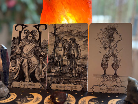 Three tarot cards on a table featuring intricate designs: The Emperor, Knight of Pentacles, and Temperance. A soft warm light glows behind.