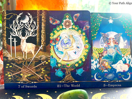 Three tarot cards on a bright altar: 7 of Swords, 21 The World, and 3 Empress, with deer, angels, and butterflies.